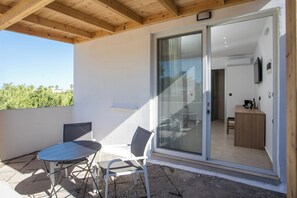 A balcony with a table and chairs, a sliding glass door leading to an interior room, and a wooden ceiling. - PADO LIVING (Faliraki)