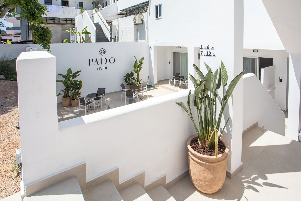 A white building with a sign that reads 'PADO LIVING' and a potted plant.