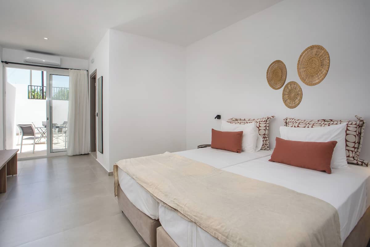 A modern hotel room with a large bed, two pillows, a bench, and a view of the outdoor area.