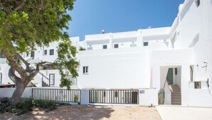 Un bâtiment blanc avec un escalier menant à l’entrée, une allée bordée de portails et un arbre au premier plan.