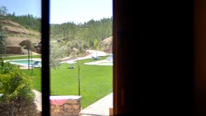 Vista attraverso una finestra su una zona erbosa con piscina, alberi e un muro di pietra.