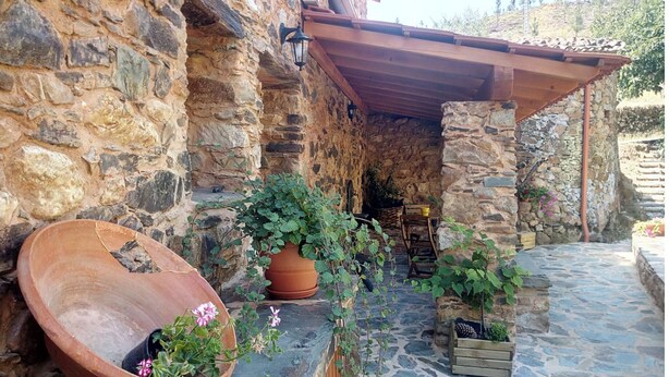 Un edificio in pietra con una pergola in legno, vasi in terracotta e un vialetto in pietra.