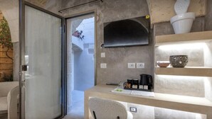 Ein modernes Zimmer mit Glastür zum Balkon, einem kleinen Schreibtisch mit Stuhl, einer Kaffeemaschine und Dekoration auf Regalen.