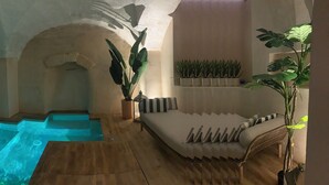 Ein Wellnessbereich mit Whirlpool, Holzboden, einer Couch und Topfpflanzen.