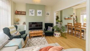 A living room with a TV, sofa, chairs, a coffee table, and a dining area with chairs and a table.