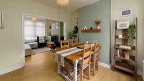 A dining area with a wooden table and chairs, a hanging light fixture, and a bookshelf with books and decorative items.