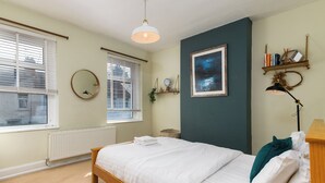 A bedroom with a wooden bed, white bedding, a night sky painting, a round mirror, and a radiator.