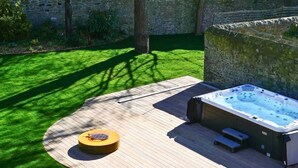 A hot tub on a wooden deck with a circular seating area, surrounded by a stone wall and greenery.