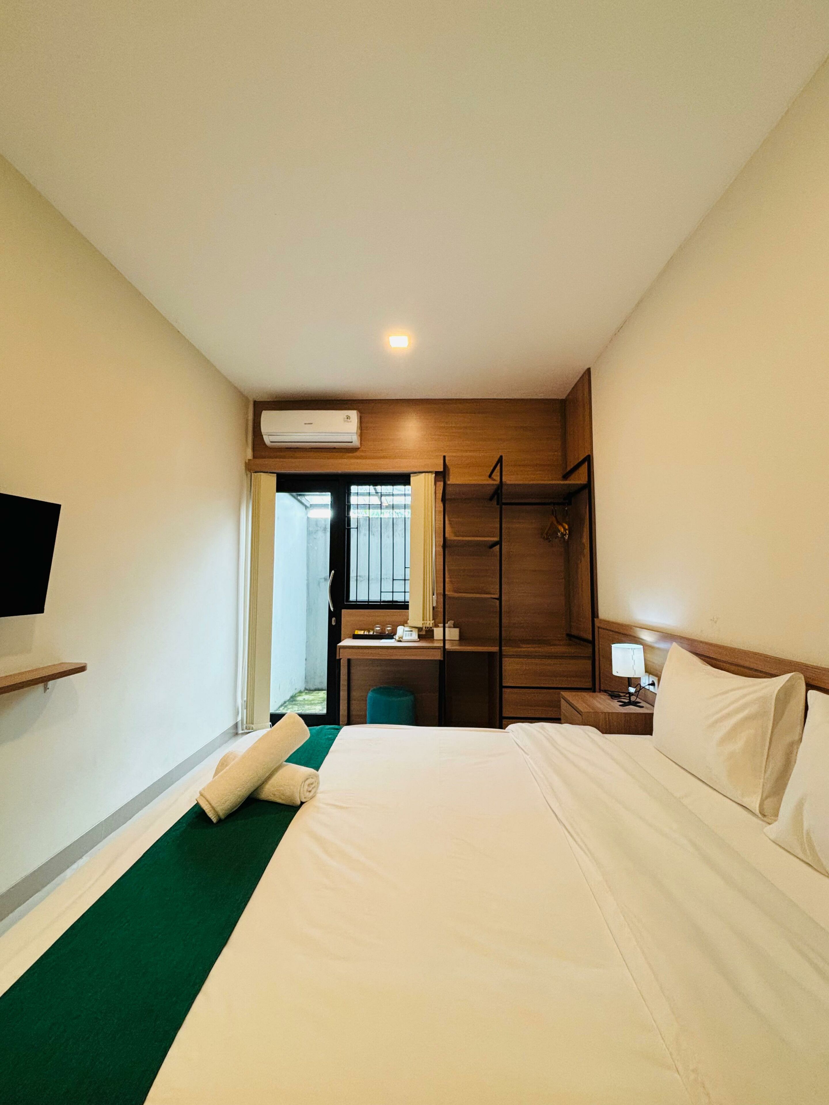 Ein Hotelzimmer mit einem Bett, einem Schreibtisch, einem Stuhl, einem Fernseher und einer Klimaanlage.