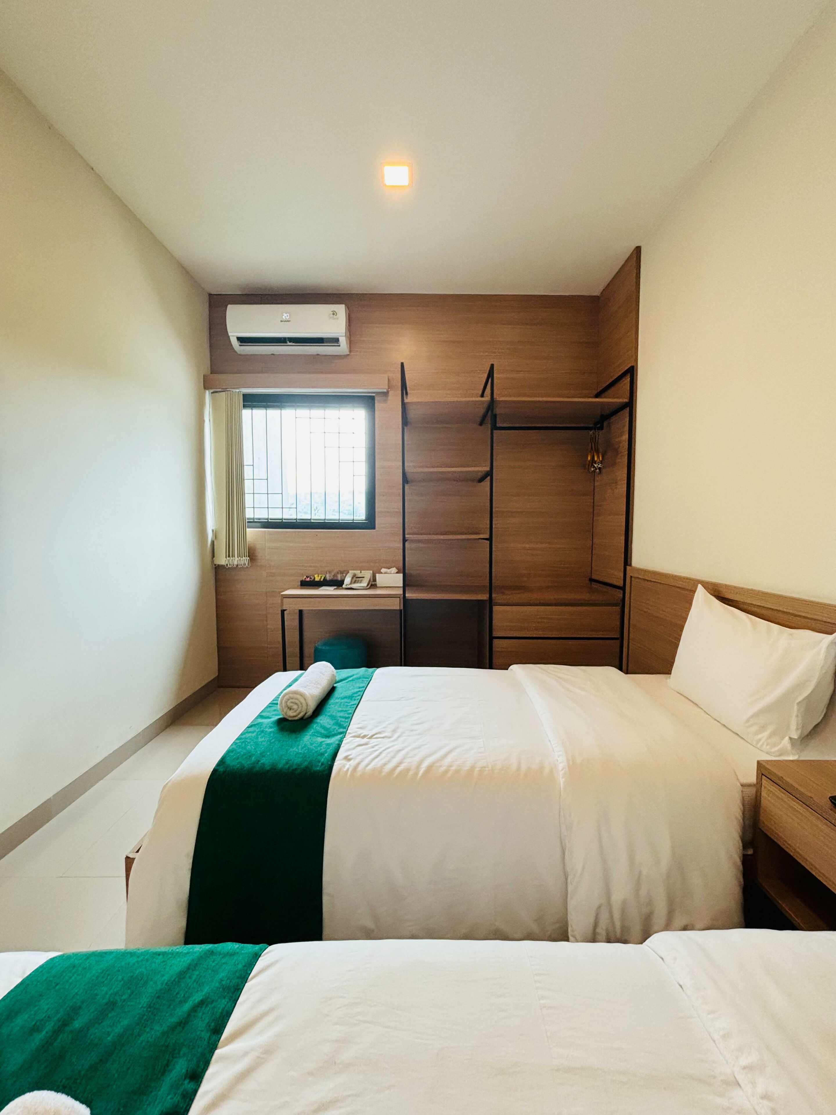A hotel room with two beds, a desk with a chair, a ladder, and a window with blinds.