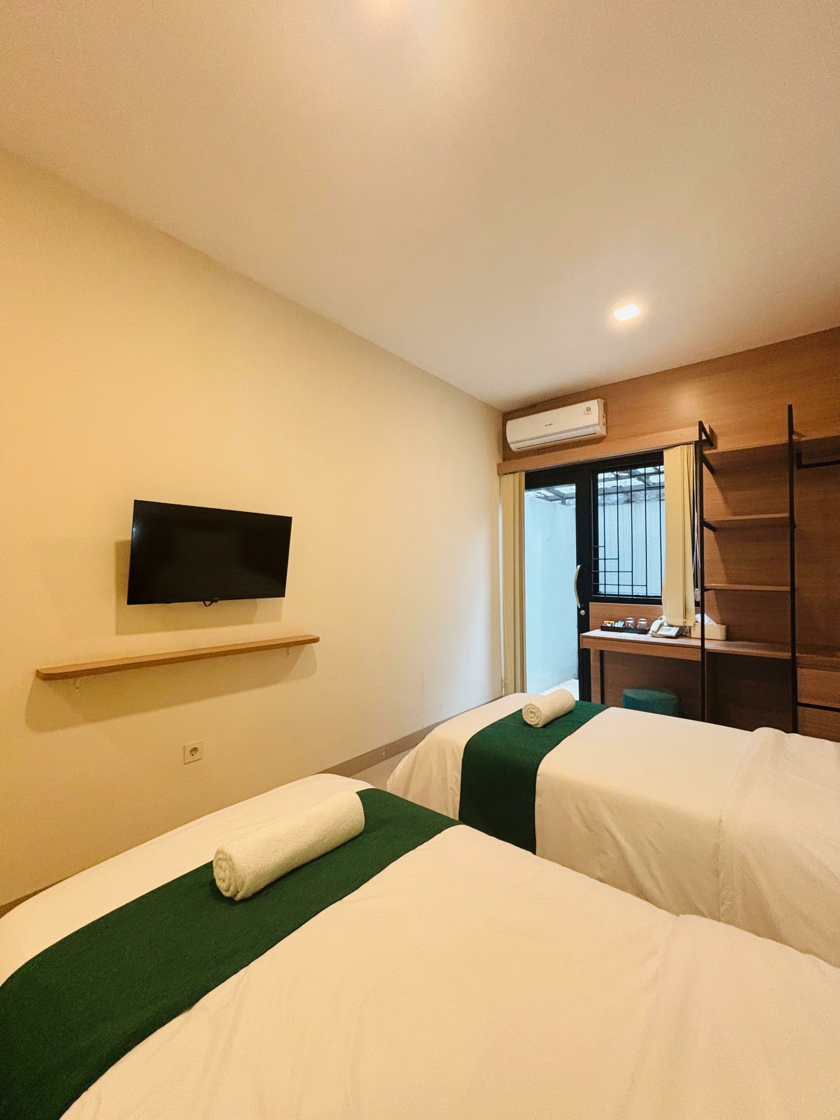 Una habitación de hotel con dos camas, un televisor montado en la pared, un escritorio con una silla y un equipo de aire acondicionado.