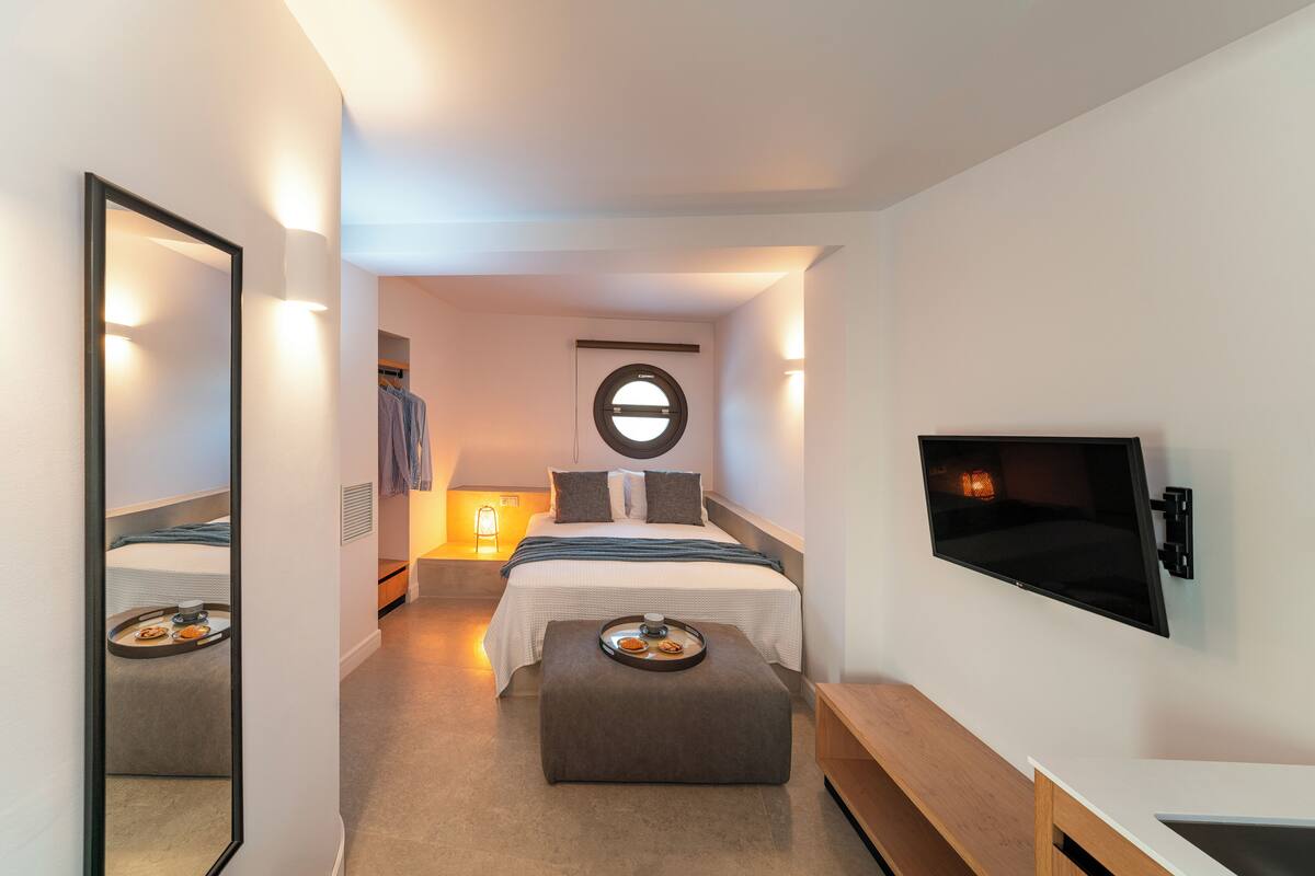 Una moderna camera d'albergo con un letto, una TV, uno specchio, un comodino e un vassoio con prodotti per la colazione.
