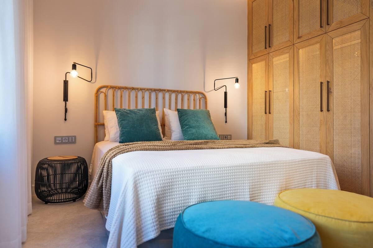 Una camera da letto con un letto, due luci a parete, un tavolino rotondo e un armadio con motivo intrecciato.