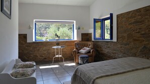 Een slaapkamer met een bed, een stoel, een tafeltje en een raam met uitzicht op groen.