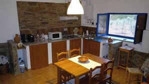 Een kleine keuken met een achterwand van steen, houten kastjes en een eethoek met een tafel en stoelen.