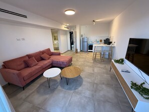Una sala de estar moderna con un sofá seccional rosa, una mesa de centro redonda y un televisor sobre un mueble blanco.