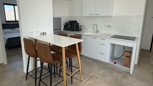 A modern kitchen with white cabinets, a dining table with four chairs, a built-in oven, and a sink.