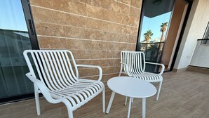 A modern outdoor seating area with two white chairs and a small table, set against a brick wall with a glass door leading to a balcony.