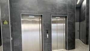 Two elevator doors in a modern hallway with dark tiles and a light floor.
