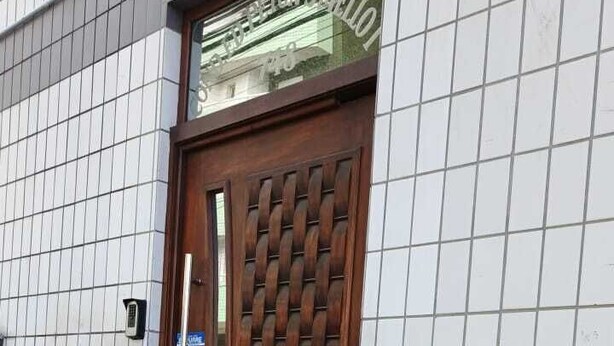 Ein Gebäude mit einer Kachelfassade, einer Holztür mit Metallgitter und einer kleinen Treppe zum Eingang.