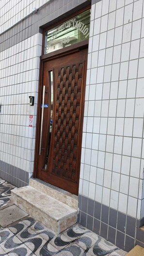 A building with a tiled exterior, a wooden door with a metal grid, and a small set of steps leading to the entrance. - KitTop Praia Grande (Cidade Ocian Praia Grande)