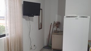 Eine kleine Küche mit einem Kühlschrank, einem an der Wand montierten Fernseher und einem Fenster mit Vorhängen.