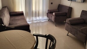 A living room with a sofa, armchairs, a TV mounted on the wall, and a dining table with chairs. - Erden Homes (Marmaris)