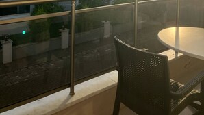Un balcone con tavolo e sedie, affaccia su una zona residenziale con edifici e cielo sereno.