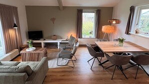 A spacious living area with a sofa, chairs, a dining table, and a TV.
