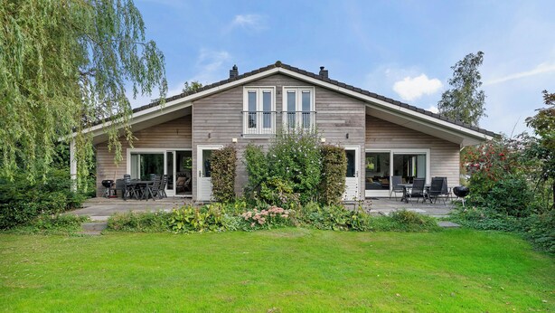 A two-story house with a covered patio, a lawn, and a garden with various plants and flowers.