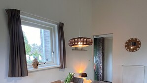 A dining area with a wooden table, four grey chairs, a hanging light fixture, a window with curtains, and a radiator on the wall.