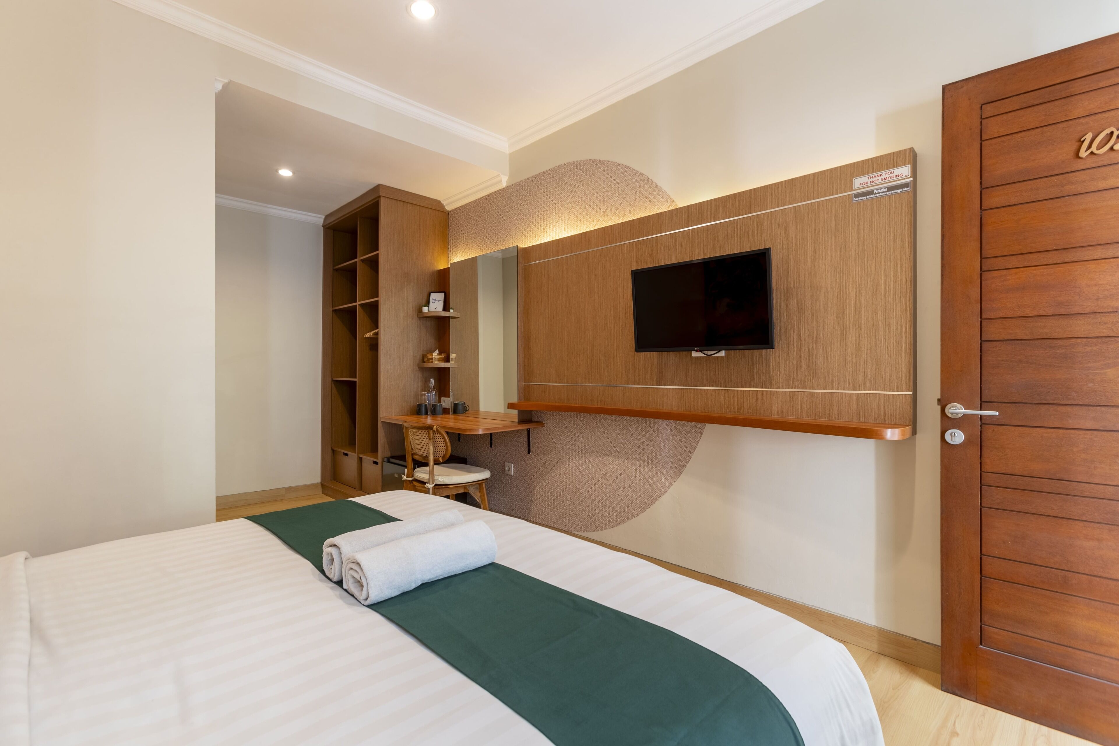 Habitación de hotel con cama, televisor montado en la pared, armario de madera y estantería empotrada.