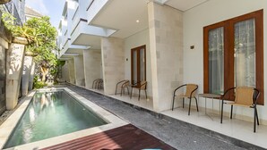 A pool area with a wooden deck, lounge chairs, and a tiled walkway. - Cove Vin Stay (Denpasar)