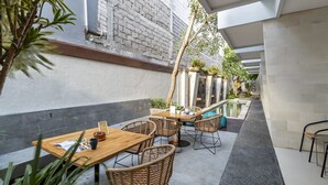 An outdoor patio with tables and chairs, a small pool, and potted plants. - Cove Vin Stay (Denpasar)