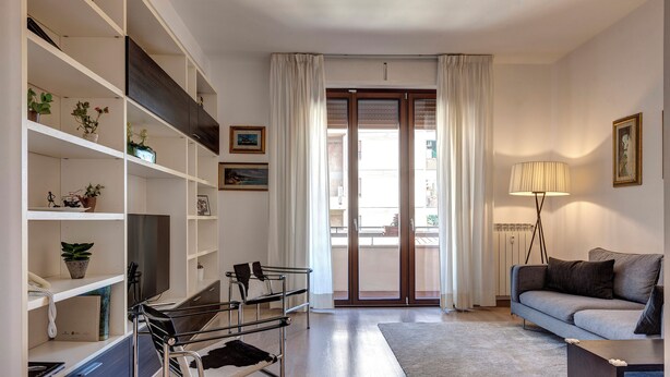 Un salon moderne avec un canapé, une lampe, une bibliothèque et une porte-fenêtre coulissante donnant sur l’extérieur.
