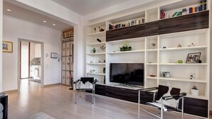 Un salon moderne doté d’un grand téléviseur à écran plat, d’étagères intégrées où sont disposés des livres et des objets décoratifs, d’un canapé et d’une table basse.