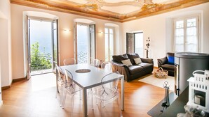 Un salon spacieux doté d’une cheminée, un coin repas avec des chaises transparentes et de grandes fenêtres offrant une vue sur l’extérieur.