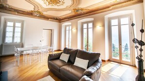 Un salon spacieux avec un canapé en cuir marron, une table à manger avec des chaises, de grandes fenêtres et un plafond décoratif.