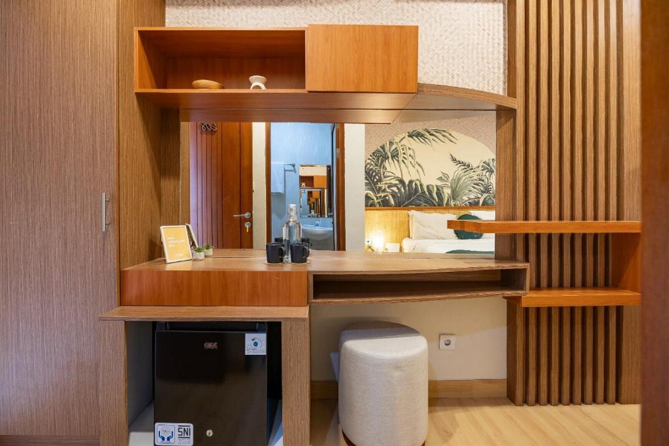 A compact kitchenette with a built-in dishwasher, a small stool, and a wooden shelf with a tropical mural.