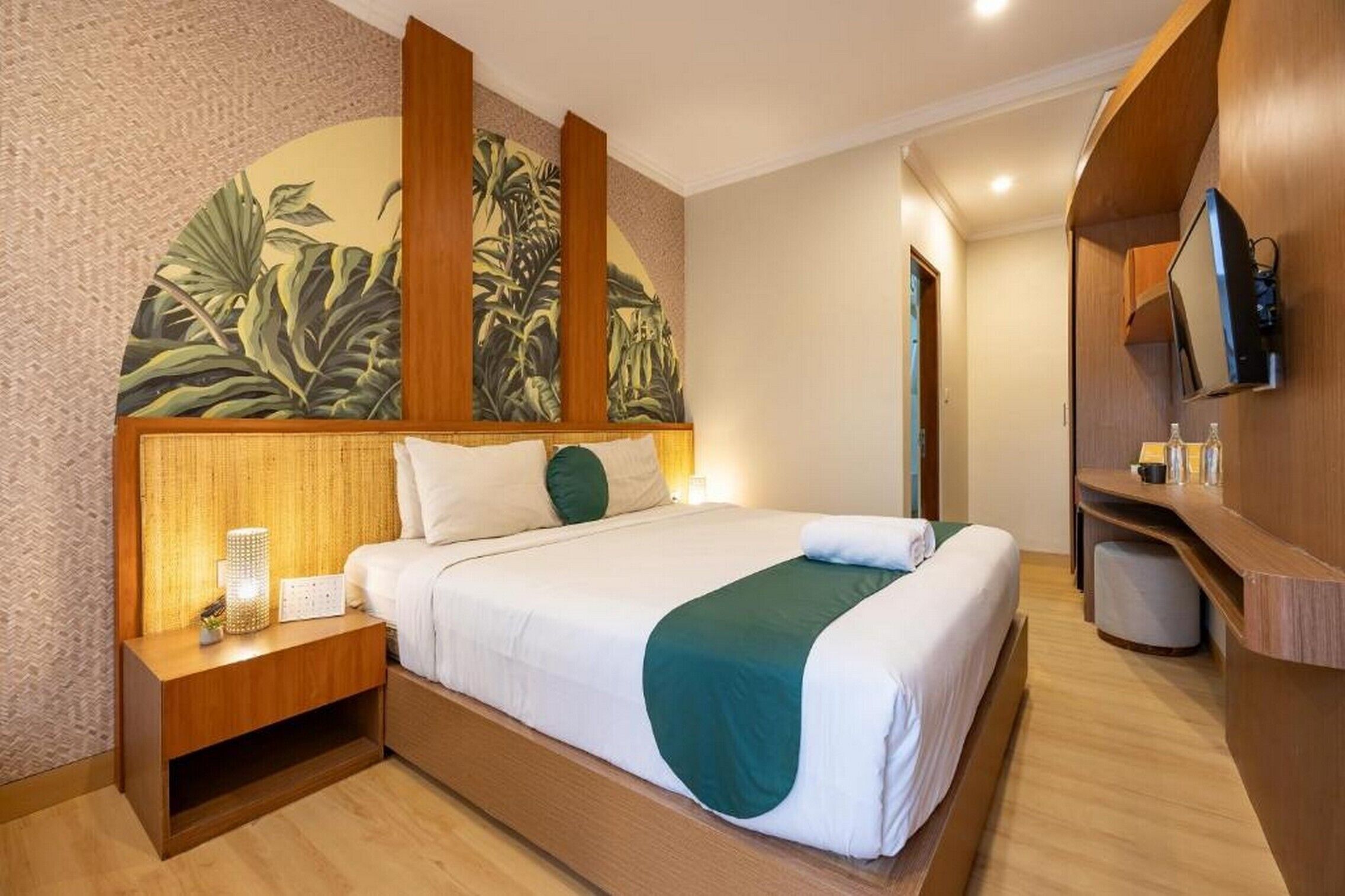 A hotel room with a large bed, a nightstand, a TV, and a wall with a tropical mural.