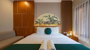 Un letto rifatto con due asciugamani arrotolati, una coperta verde e un murale tropicale al muro.