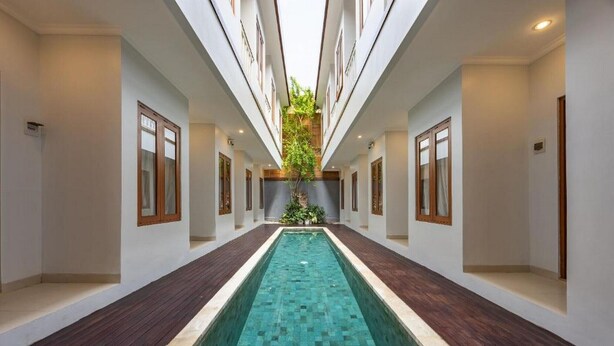 Una piscina interna stretta con pavimento in legno, circondata da pareti bianche e finestre con cornice in legno.