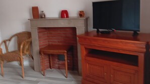 Habitación de hotel con cama, un mueble de televisión de madera, televisor, sillón de mimbre, una mesita y chimenea.