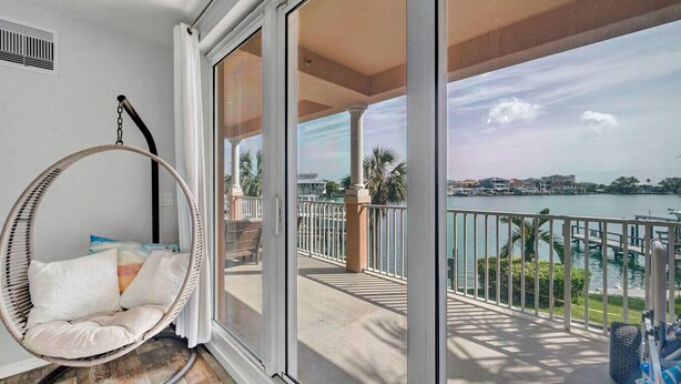 A balcony with a hanging chair, a view of the water, and a building in the background.