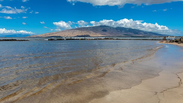 A beach with clear water, a rocky shoreline, and a mountain in the background. - Menehune Shores, #609 2 Bedroom Condo (Kihei)