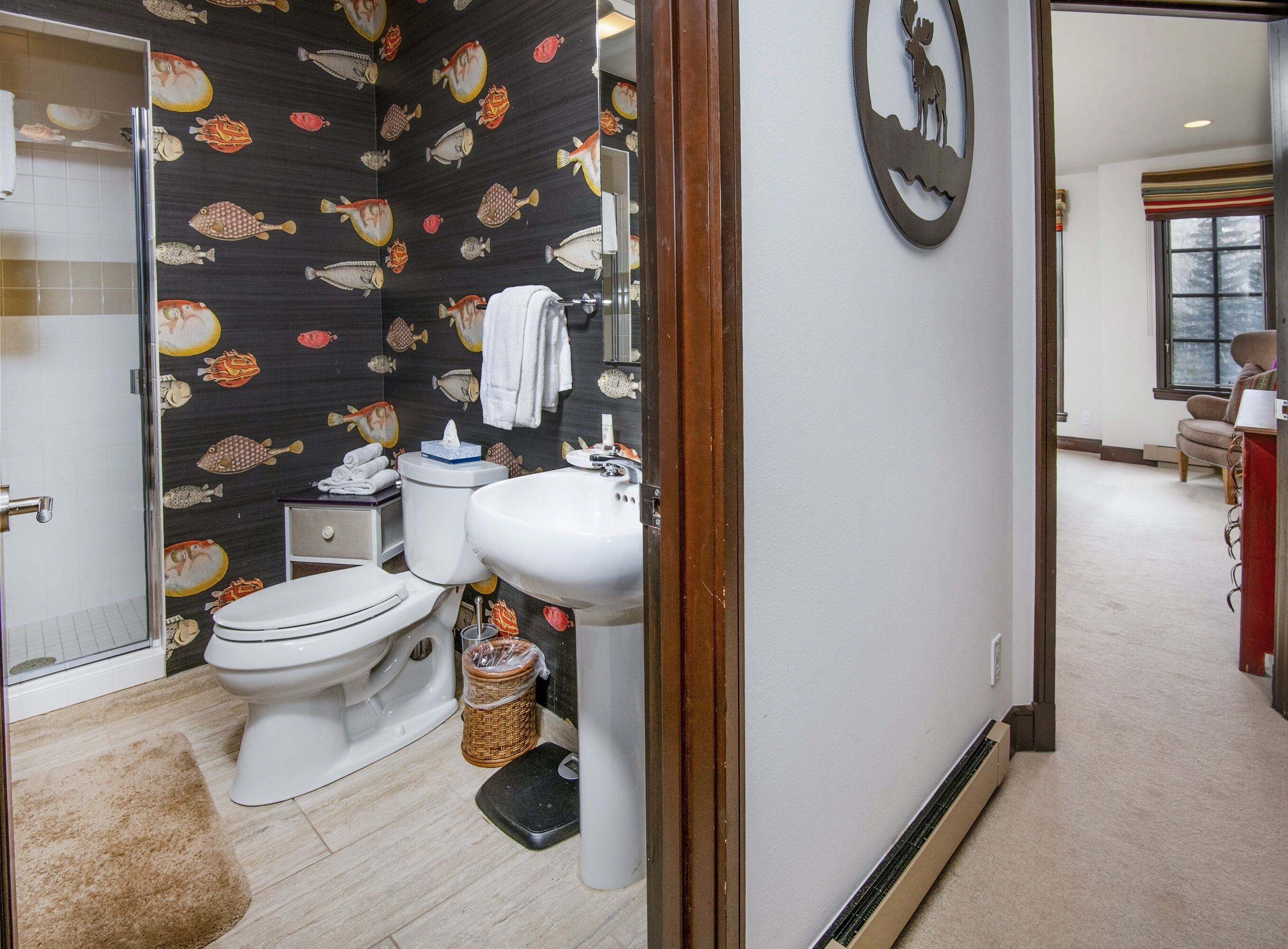 Un baño con inodoro, lavamanos y zona de ducha. Se aprecia una pared con diseño y una ventana al fondo.