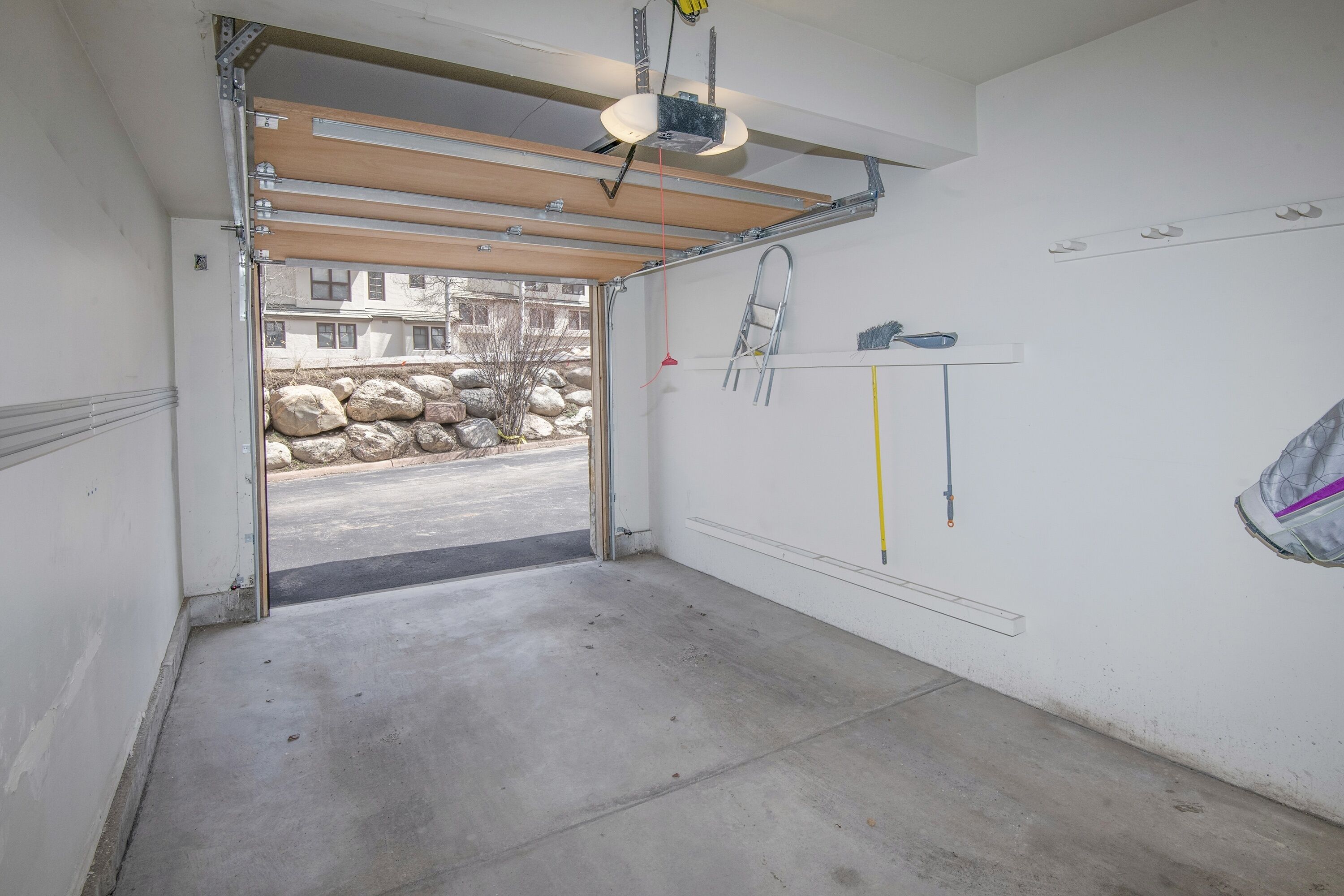 A garage with a concrete floor, a wooden door, and a metal ladder leaning against the wall.