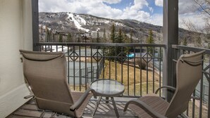 Ein Balkon mit zwei Stühlen und einem kleinen Tisch, der einen Blick auf eine Berglandschaft mit Skipiste und See bietet.