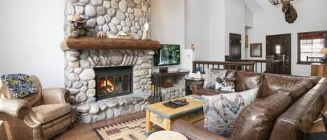 Una sala de estar acogedora con chimenea de piedra, muebles de cuero y un ciervo colgado en la pared.
