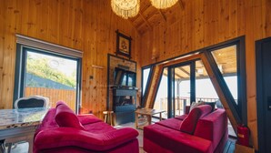Ein Holzhütten-Innenraum mit Kamin, roten Sofas, einem Esstisch und großen Fenstern mit Blick ins Freie.